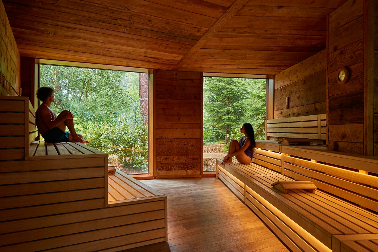 Man and woman sitting enjoying the forest views from inside the Nordic Sauna.